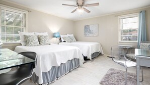 A bedroom with two beds, a desk, a chair, a ceiling fan, and a window with blinds.
