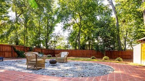 A patio area with a brick floor, two wicker chairs, a fire pit, and a wooden fence.