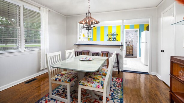 A dining area with a table and chairs, a hanging light fixture, and a colorful rug.