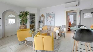Una sala de estar moderna con un sofá amarillo, un sillón blanco y una zona de comedor con mesa y sillas.