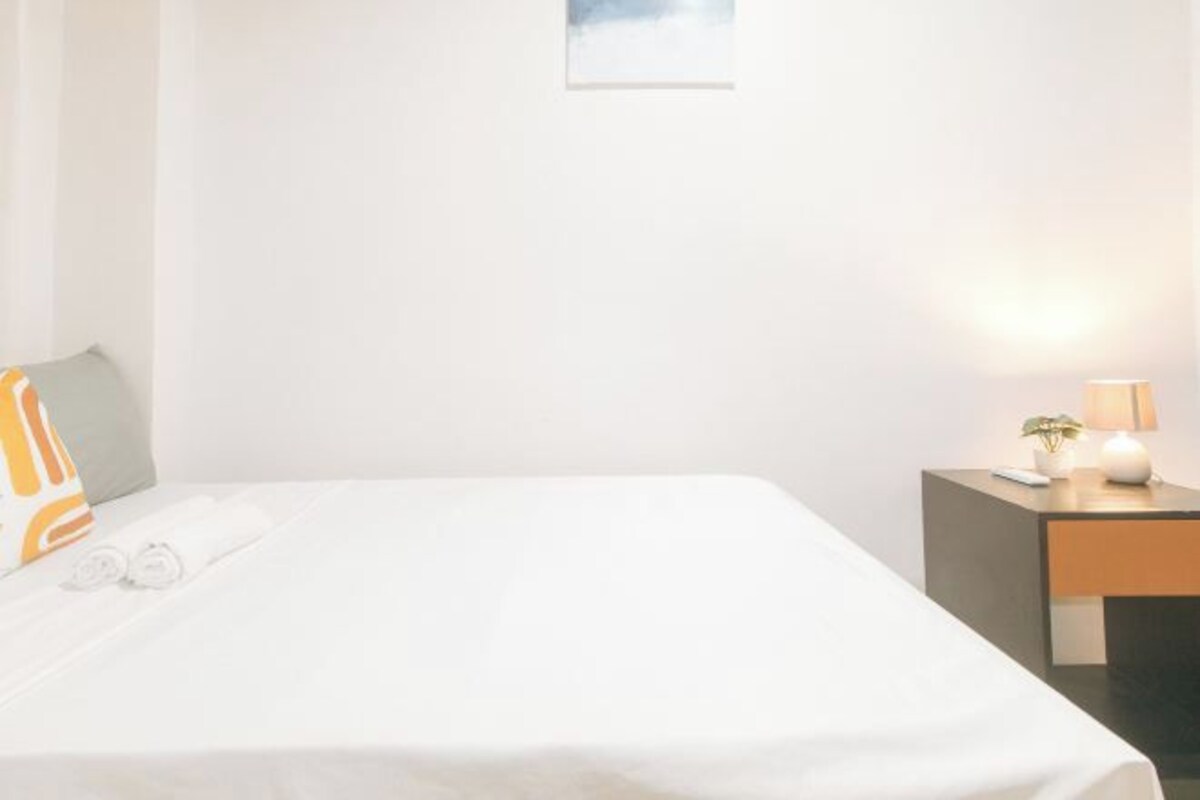 Habitación de hotel con una cama, una mesita de noche con lámpara y una pequeña mesa con planta.