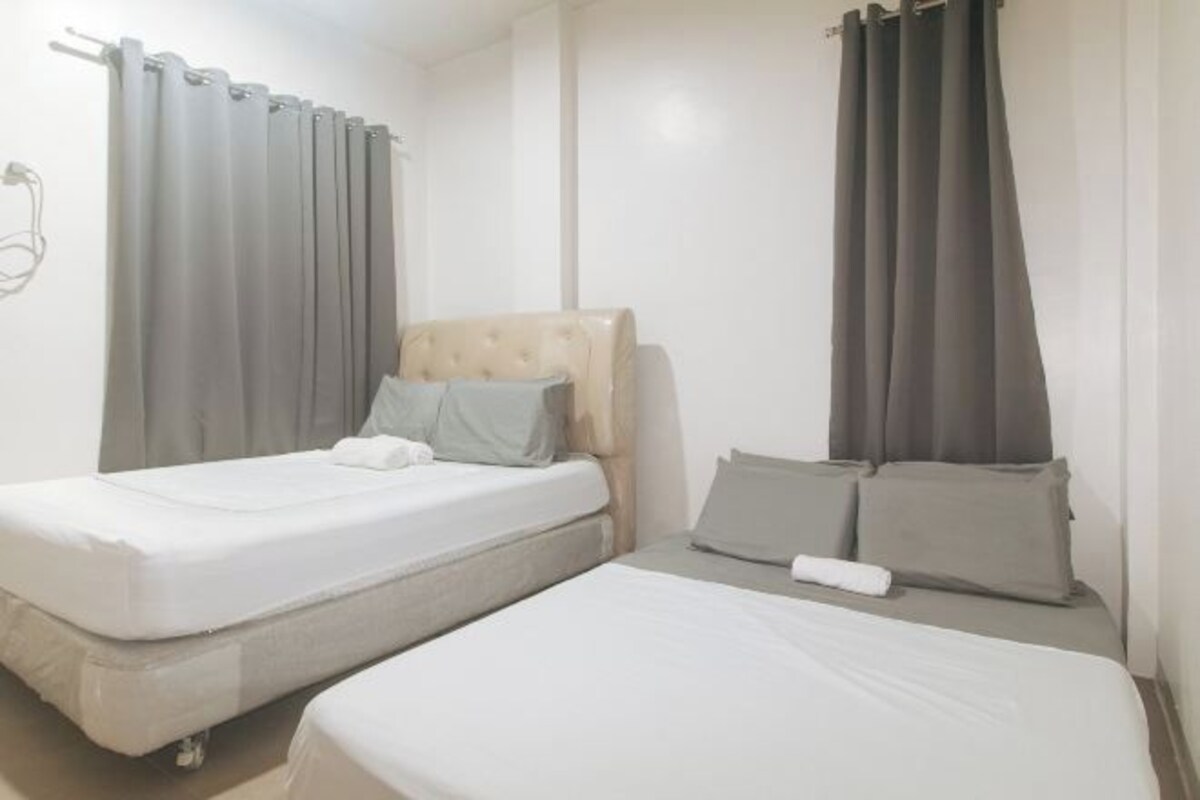 A hotel room with two beds, grey curtains, and a beige headboard.