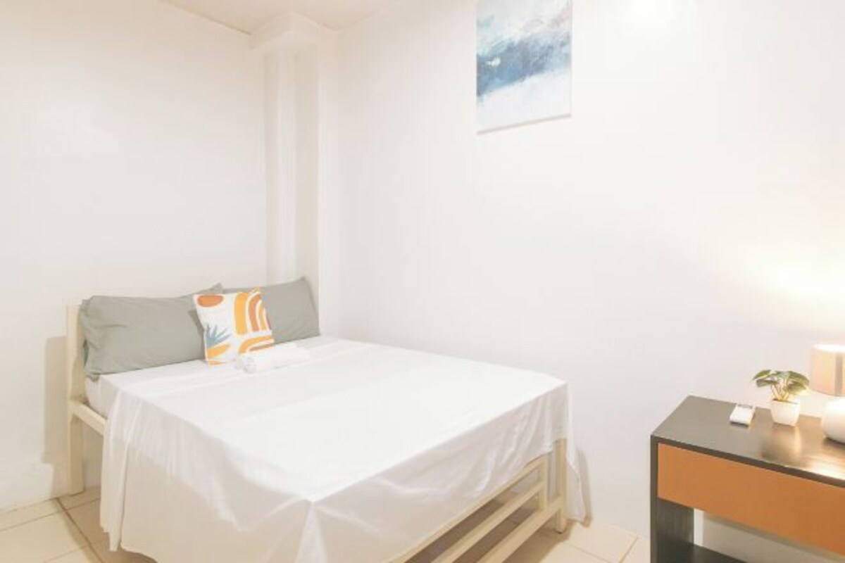 A small, clean room with a bed, a bedside table, and a small plant.
