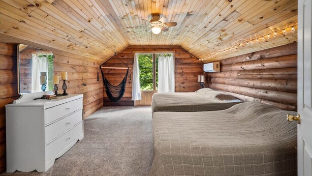 Un dormitorio tipo cabaña de madera con cama, cómoda, hamaca colgante y ventilador de techo.