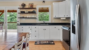 Una cocina con armarios blancos, encimera negra y refrigerador de acero inoxidable.