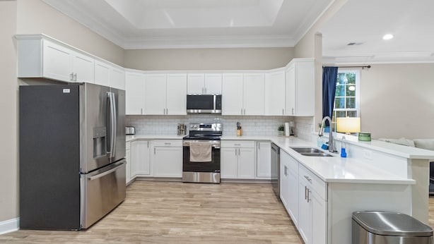 A modern kitchen with white cabinetry, stainless steel appliances, and a wooden floor. - Home the way you need it. (Lexington)