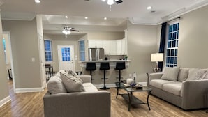 A modern living room with a gray sofa, a glass coffee table, and a kitchen in the background. - Home the way you need it. (Lexington)