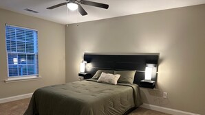 A bedroom with a bed, a ceiling fan, a nightstand with a lamp, and a window with blinds. - Home the way you need it. (Lexington)