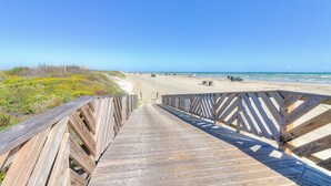 Ein Holzsteg führt zu einem Strand unter blauem Himmel.