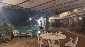 An outdoor patio area with a pool, white metal chairs, and tables. - Casa del Roble 2 Residence (Cuernavaca)