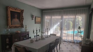 A dining room with a table set for four, a large framed portrait, and a view of a swimming pool through sheer curtains. - Casa del Roble 2 Residence (Cuernavaca)