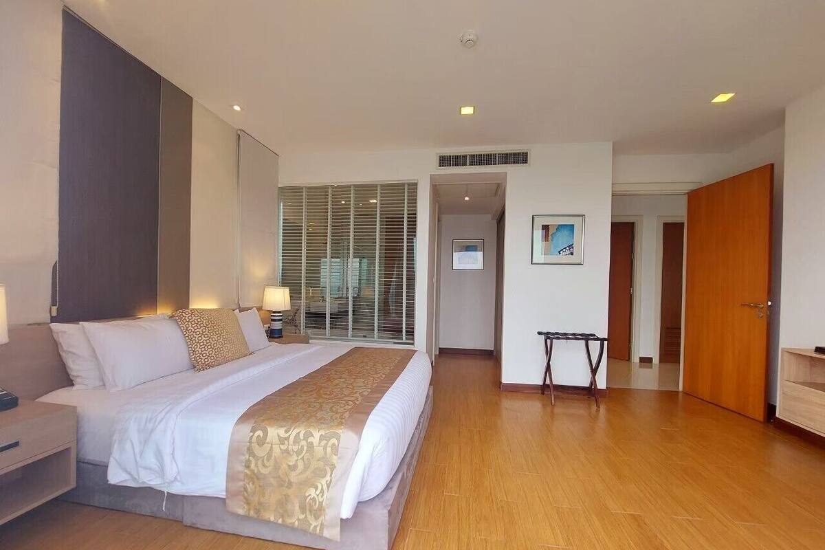 A hotel room with a large bed, bedside tables, a desk, a chair, a window with blinds, a door, and a small table.