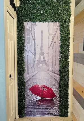 Una puerta con un mural de una calle parisina, que incluye la Torre Eiffel y un paraguas rojo.