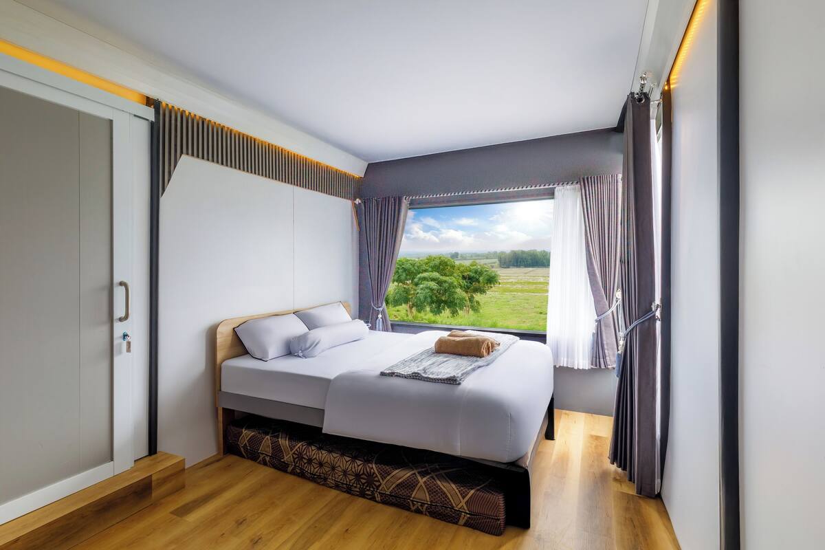 A bedroom with a bed, a wardrobe, and a view of the outdoors.