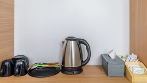 Un comptoir de cuisine avec une bouilloire en acier inoxydable, une bouilloire électrique noire, une théière et une boîte de mouchoirs.