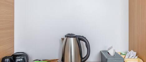 A kitchen counter with a stainless steel kettle, a black electric kettle, a tea kettle, and a box of tissues.