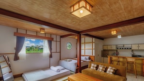 Une pièce de style japonais traditionnel, avec un sol recouvert de tatamis, un lit bas en bois, un canapé et un coin cuisine doté de meubles en bois et d’un tabouret de bar.