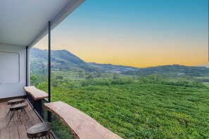 A balcony with wooden furniture overlooking a lush green landscape and distant hills. - Fortune Cube (Kejajar)