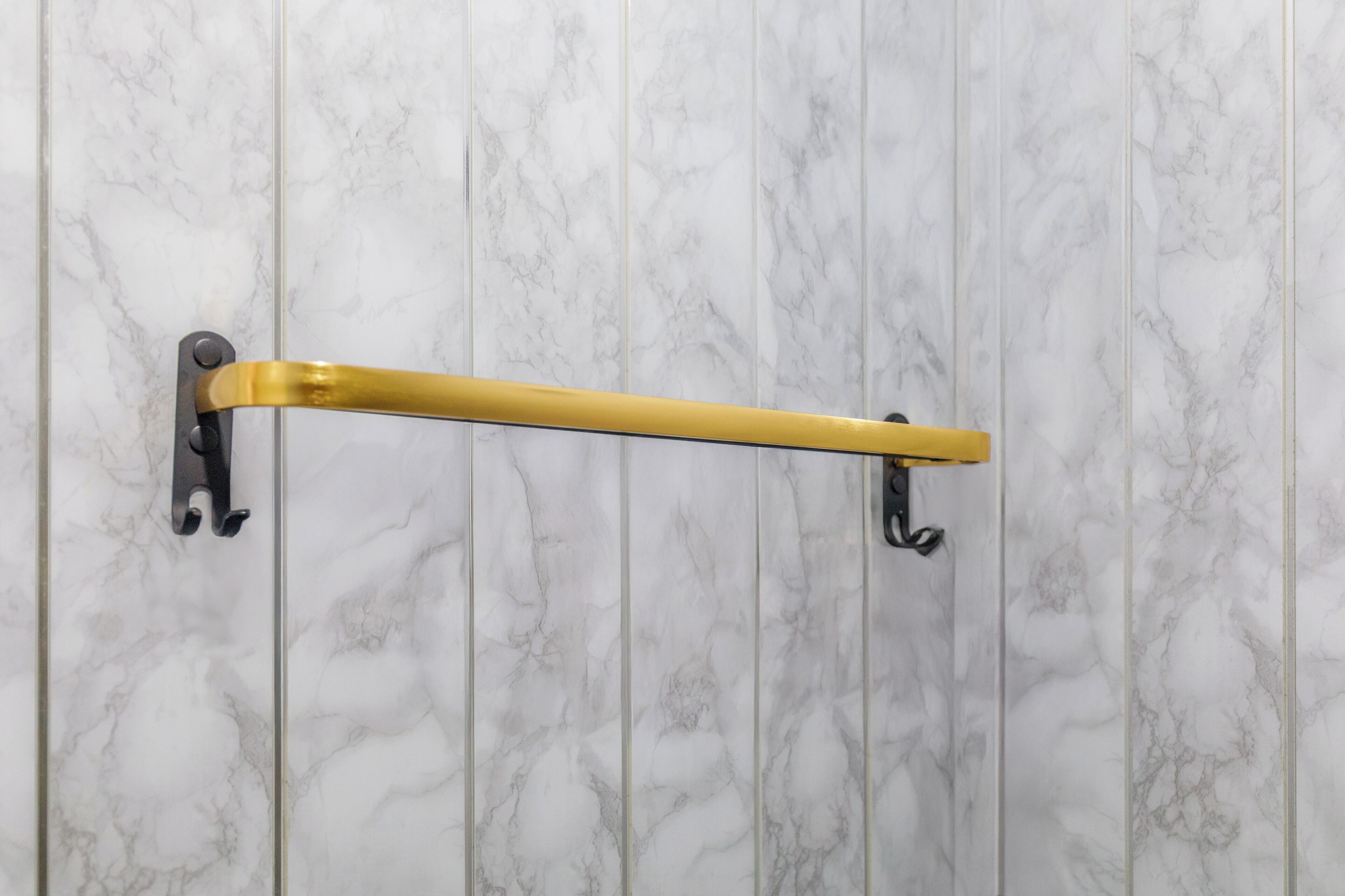 Uma casa de banho com parede de mármore e porta-toalhas dourado.