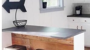 Een keuken met een houten keukeneiland, twee krukken, een zwarte hanglamp en een raam met uitzicht.