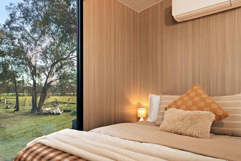 Un dormitorio con un ventanal grande, una cama con una manta mullida y una mesita de noche con lámpara.