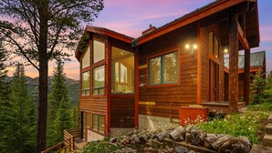Una cabaña de madera con ventanas amplias, una terraza y vistas al bosque circundante.