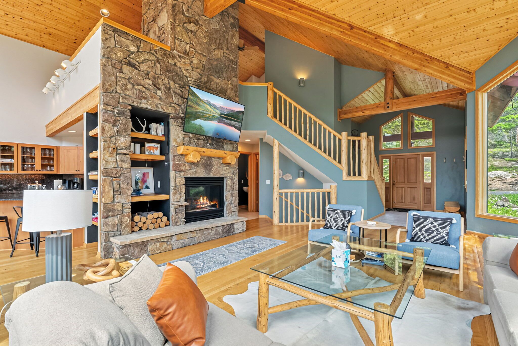 A spacious living area with a stone fireplace, wooden beams, and a large TV.
