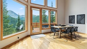 Una habitación con ventanas amplias, una mesa de madera con sillas y vistas a las montañas.