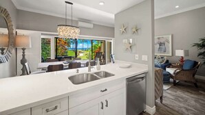 Una cocina moderna con una isla grande, electrodomésticos de acero inoxidable y vistas a un paisaje tropical.