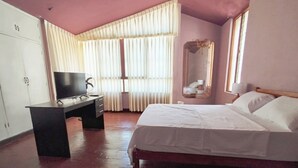 A bedroom with a bed, a desk with a TV, a wardrobe, and a window with curtains.