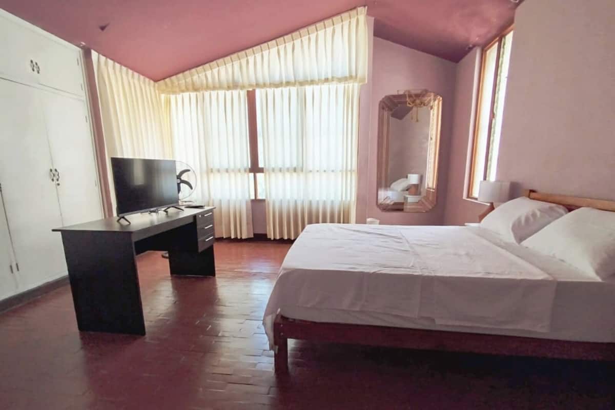Ein Schlafzimmer mit einem Bett, einem Schreibtisch mit Fernseher, einem Kleiderschrank und einem Fenster mit Vorhängen.