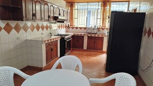 A kitchen with wooden cabinets, a stove, and a refrigerator. There are two white plastic chairs and a small table.