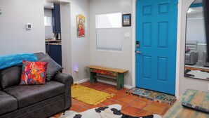 A living room with a gray couch, colorful pillows, a wooden bench, a blue door, and a patterned rug.