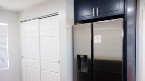 A kitchen with a stainless steel refrigerator, a double door closet, and dark cabinets.