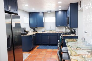 Une cuisine moderne avec des meubles de couleur bleu foncé, un réfrigérateur en acier inoxydable, un pare-feu en carrelage et un grand îlot central doté d’un comptoir en granit.