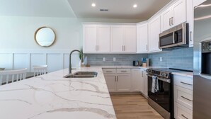 A modern kitchen with white cabinets, a marble island, stainless steel appliances, and a tiled backsplash. - 4bedroom,5bed,4bath, elevator, ocean views and golf cart (Surf City)