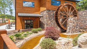 Un bâtiment en bois doté d’une grande roue à eau, d’un mur en pierre et d’un petit étang planté de végétaux.