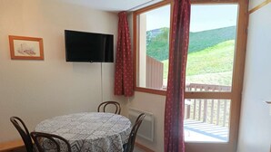 A dining area with a table and chairs, a television mounted on the wall, and a view of a balcony with a wooden railing. - Paradiski closed to the slopes and shop vallandry (LANDRY)