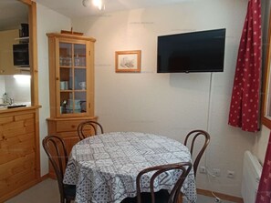 Un comedor con una mesa redonda, sillas, un armario con puertas de cristal, un televisor montado en la pared y una cortina roja.