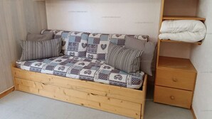 Un canapé en bois avec des coussins à motifs, dans une pièce dont le sol est recouvert de carreaux et qui contient un meuble en bois.