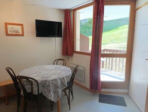 A dining area with a table and chairs, a television mounted on the wall, and a view of a green landscape through a window. - Paradiski closed to the slopes and shop vallandry (LANDRY)