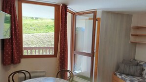 A room with a dining table, chairs, a sofa, a TV, and a sliding glass door leading to an outdoor area with a view of greenery. - Paradiski closed to the slopes and shop vallandry (LANDRY)