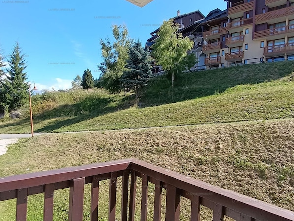 Zona residencial con una pendiente cubierta de césped, una valla de madera y edificios de varios pisos al fondo.