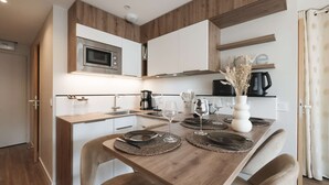 A modern kitchen with a wooden table set for dining, equipped with a microwave, coffee maker, and various utensils. - Magnificent 3-room apartment 31m², south-east facing, mountain/resort view (VAL THORENS)