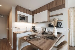 A modern kitchen with a wooden table set for dining, equipped with a microwave, coffee maker, and various utensils. - Magnificent 3-room apartment 31m², south-east facing, mountain/resort view (VAL THORENS)