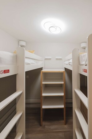 Une petite pièce avec des lits superposés, une échelle en bois au centre et un luminaire au plafond.