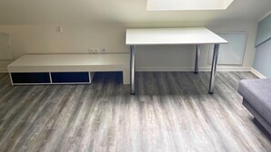 Ein Zimmer mit Oberlicht, einem weißen Schreibtisch, einer Bank und einem grauen Sofa.