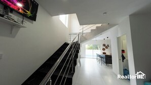 A modern interior with a staircase, a dining area, and a TV mounted on the wall. - FANTASTIC CARAIBIC VILLA in the heart of the Caribbean in the midst of nature (Sosúa)