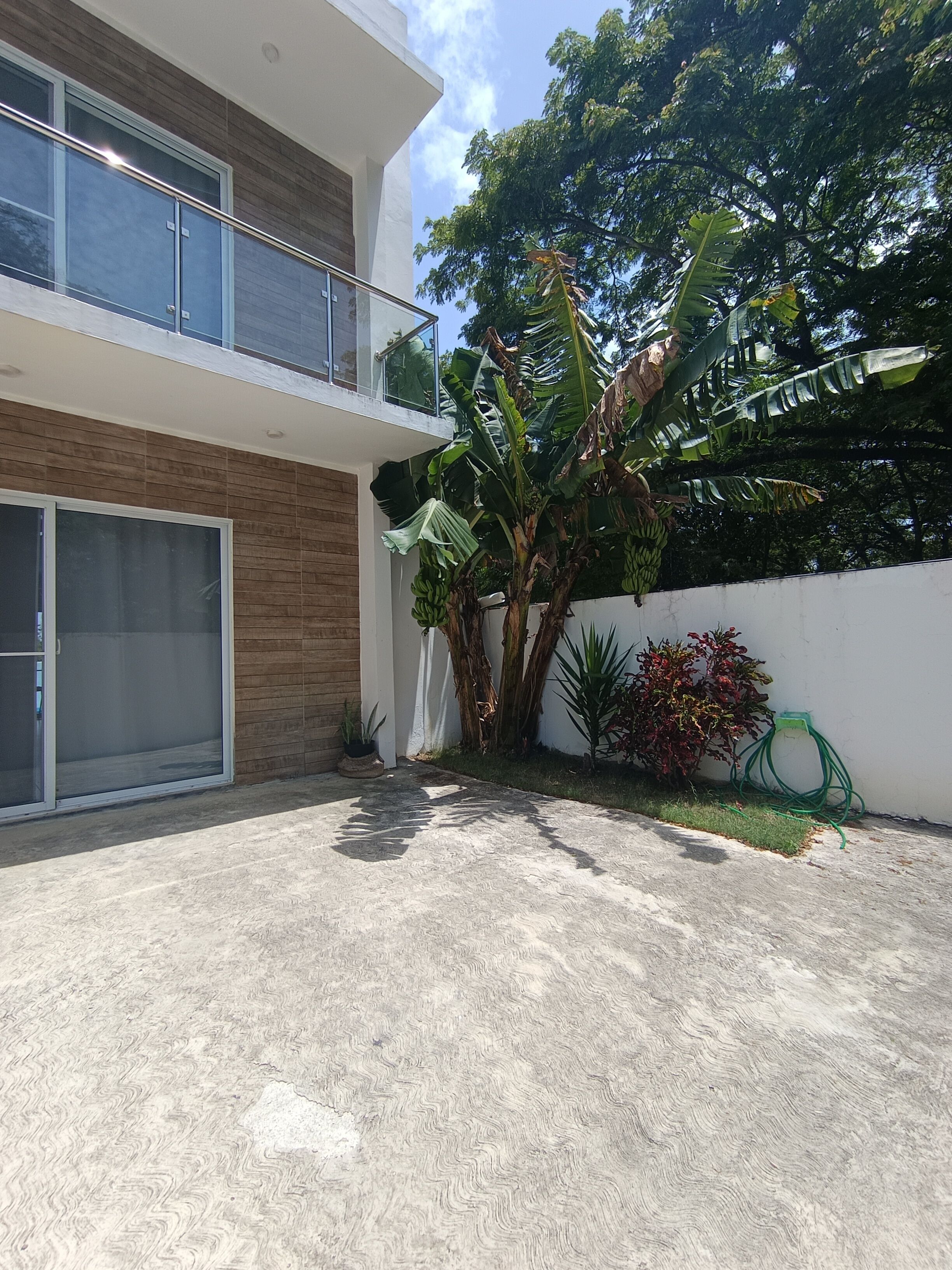 A modern two-story house with a garage, a large tree, and a garden hose.