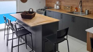 A modern kitchen with a central island, black bar stools, pendant lights, and a view of the outdoors. - FANTASTIC CARAIBIC VILLA in the heart of the Caribbean in the midst of nature (Sosúa)